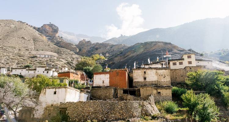 Rustic stone houses of a Himalayan mountain village set against rugged slopes and clear sky.