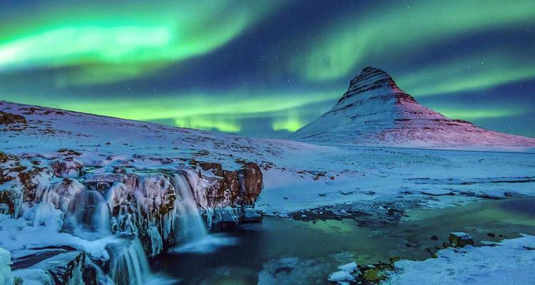Northern Lights dance over snow-covered Kirkjufell mountain and a frozen waterfall on a clear winter night.