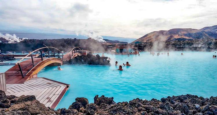 Geothermal Blue Lagoon with milky turquoise water, steam rising as bathers relax surrounded by lava fields.