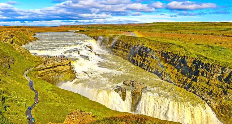 Sweeping aerial view of mighty Gullfoss waterfall thundering through a canyon, a faint rainbow visible in the spray.