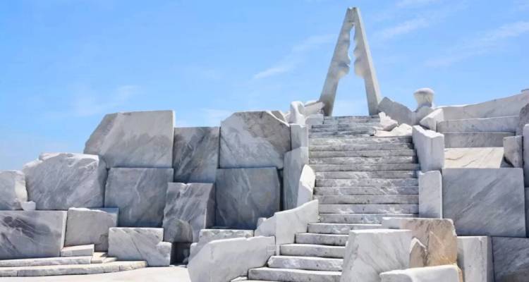 Modern abstract marble monument with angular stairs rising toward blue sky.