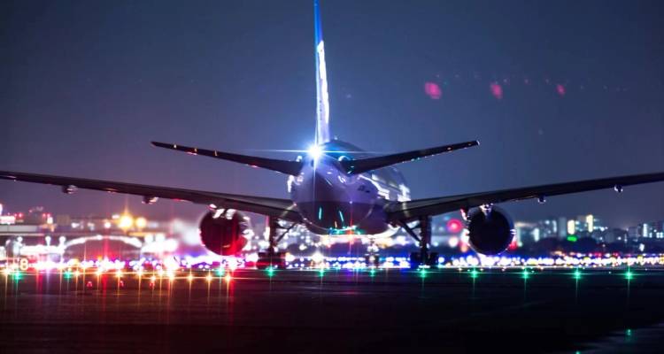 Passenger jet on illuminated runway at night with colorful taxiway lights.