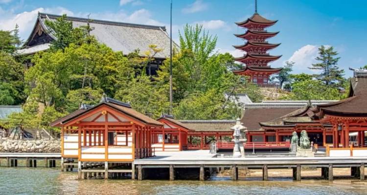 Iconic Itsukushima Shrine buildings and five-story pagoda facing calm water.