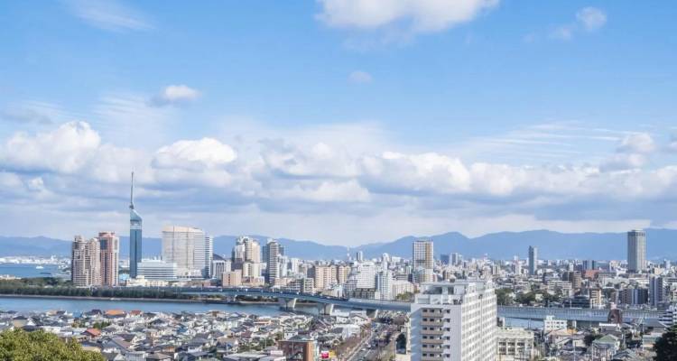 Panoramic skyline of a modern city with river, bridge and distant mountains.