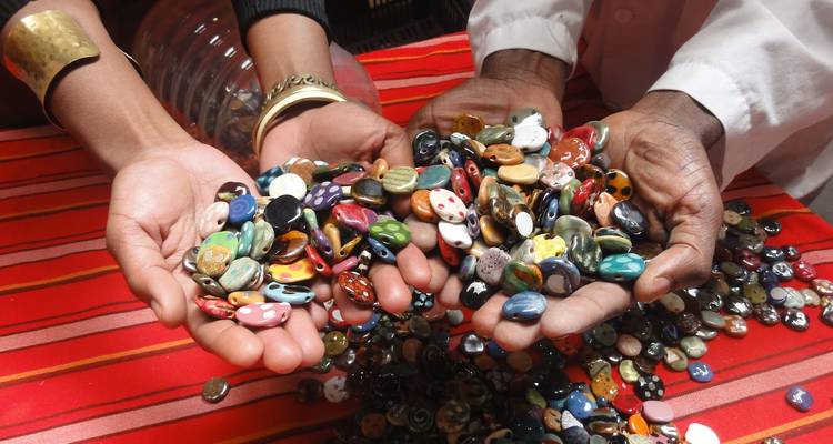 Two pairs of hands holding brightly colored ceramic beads and stones over a striped cloth