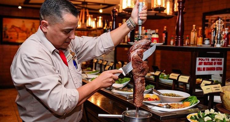Chef carving a large skewer of roasted meat in a buffet restaurant setting