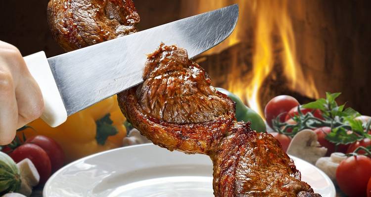 Close-up of a juicy grilled meat skewer being sliced above a white plate with vegetables