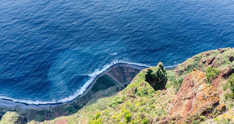 Schwindelerregende Aussicht von der Klippenkante hinab zum Atlantik, wo Wellen auf die Terrassenfelder an Madeiras Küste treffen
