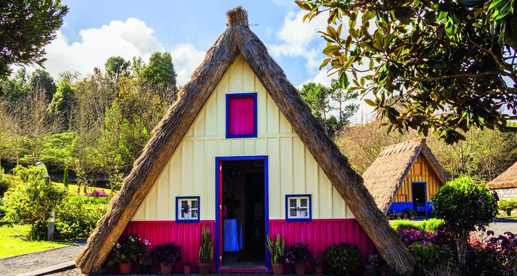Traditionelles A-Rahmen-Santana-Haus mit Strohdach und leuchtend rot und gelb gestrichenen Wänden in einem Garten