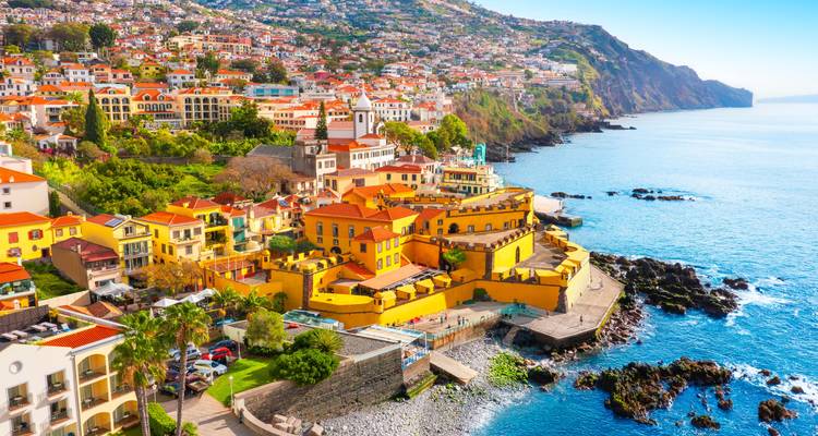 Farbenfrohe Stadtlandschaft von Funchal, die sich den Hang hinunter zum Atlantischen Ozean erstreckt.