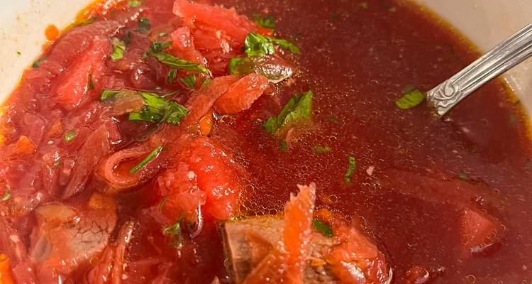 Close-up van een stevige kom rode bietensoep gegarneerd met kruiden.