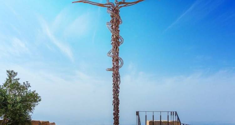 Bronzen serpentine kruissculptuur bovenop berg Nebo tegen een wazig blauwe hemel