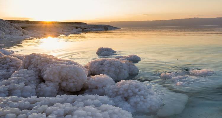 Zonsondergangslicht gloeit over kristallijne zouthopen aan de serene oever van de Dode Zee
