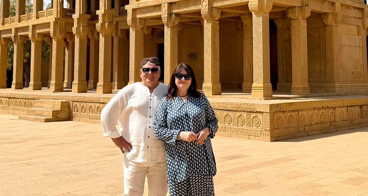 Un couple pose devant une architecture de tombeau en grès ornée sous un soleil de désert éclatant.