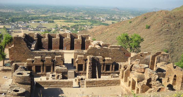 Vue du sommet d'une colline sur les ruines d'un ancien monastère bouddhiste avec une vallée et des montagnes au loin.