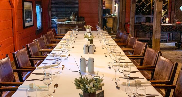 Mesa de comedor interior larga formalmente puesta con cristalería dentro de una cabaña rústica