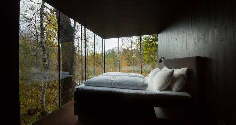 Dormitorio moderno con paredes de vidrio del suelo al techo que ofrece vista al bosque y al río