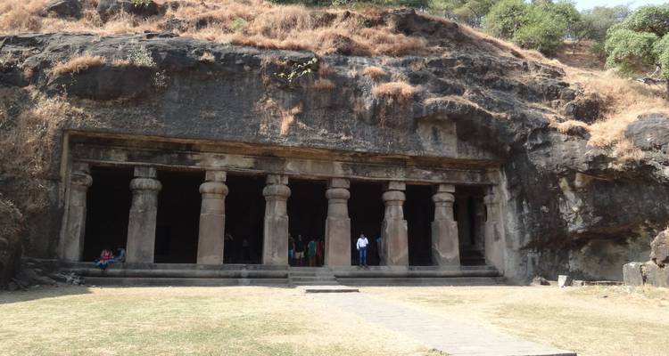 Felsengeschlagener Höhleneingang mit massiven Steinsäulen, die in einen zerklüfteten Hang eingelassen sind.