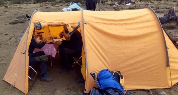 Orange expedition tent with trekkers seated at folding table eating a meal