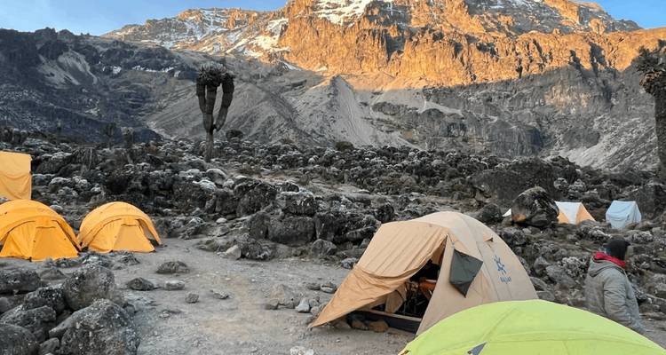 Sunlit alpine campsite beneath dramatic rocky face of Mount Kilimanjaro
