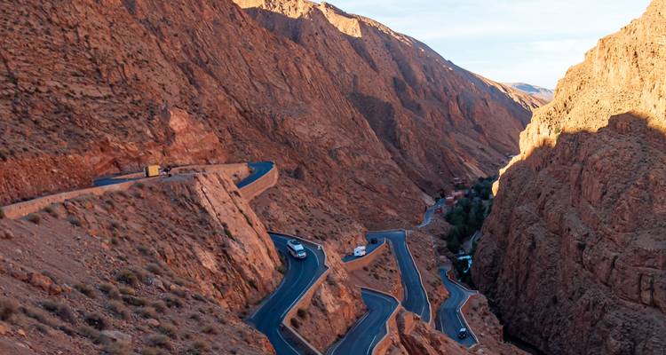 Een spectaculaire kronkelende bergweg slingert zich door steile rode rotspartijen van een nauwe kloof.