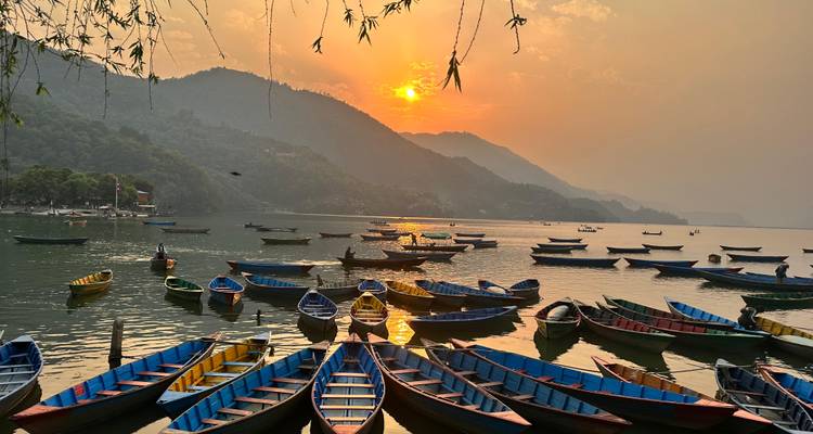 Dozens of colorful wooden paddle boats float on Pokhara's Phewa Lake at sunset beneath hazy hills