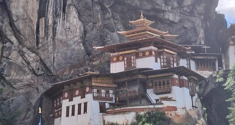 Iconic cliffside monastery with white walls and ornate golden roofs built against a dramatic rock face.