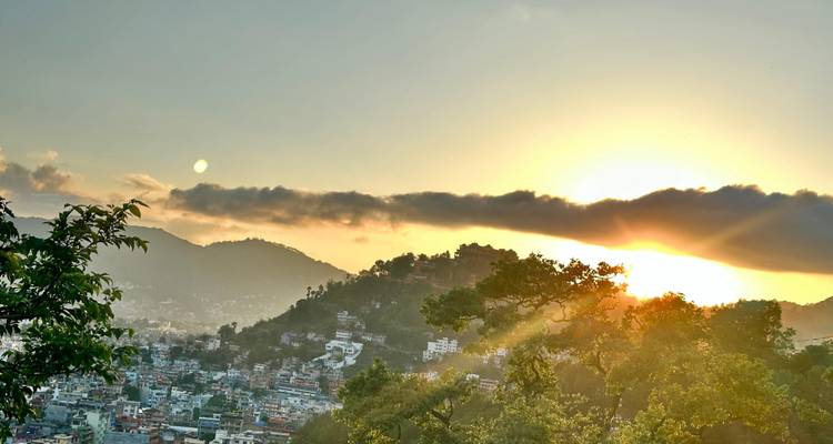 City nestled among hills at sunset with golden sun rays breaking through low clouds.