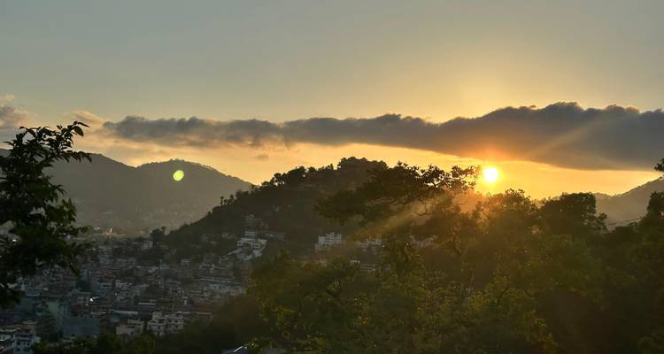 Dramatic sunset over a valley city with silhouetted hills and glowing clouds.
