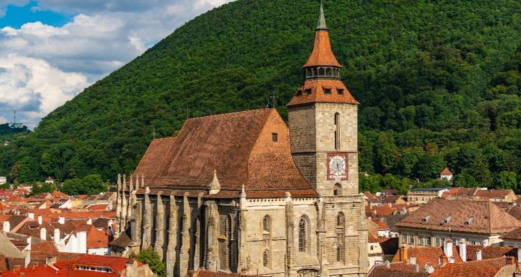 De Zwarte Kerk van Brașov die boven rode daken uitrijst met een weelderig beboste bergachtergrond