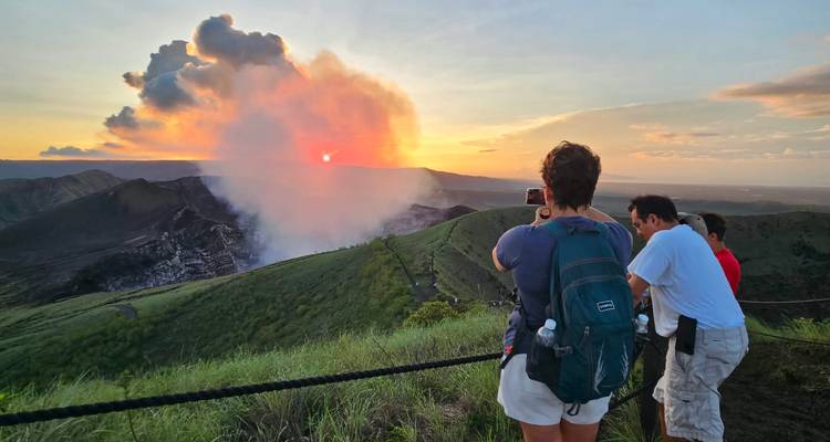 Travelers watching sunset and smoke rising from active Masaya volcano crater.