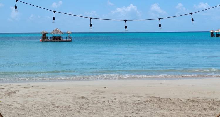 Calm turquoise sea with floating thatched cabanas viewed from a sandy beach.
