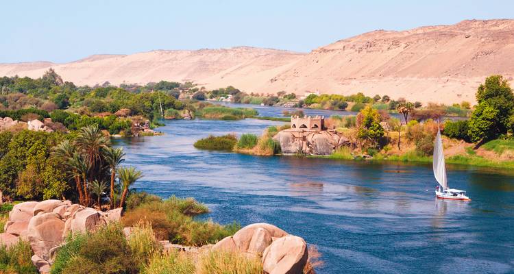 Serene stretch of the Nile with a white sailboat, green banks and desert hills beyond