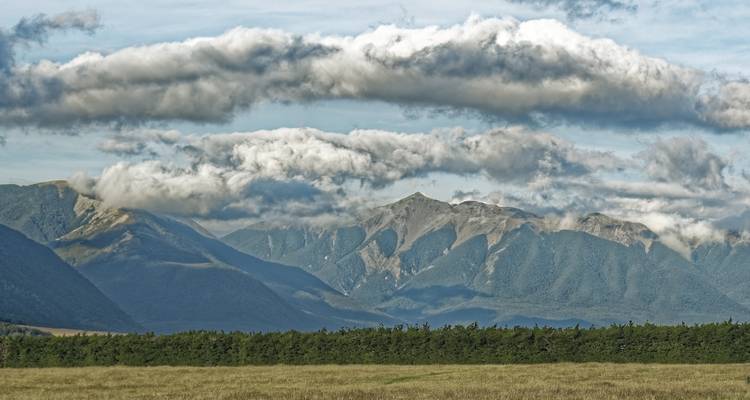 Champ avec des formations nuageuses dramatiques s'arquant au-dessus d'une chaîne de montagnes et de la lisière de forêt