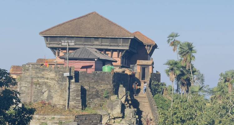 Historic hilltop palace with stone stairs and palm trees under blue sky.