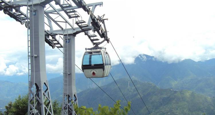 Cable car cabin travels above green mountains toward cloudy horizon.