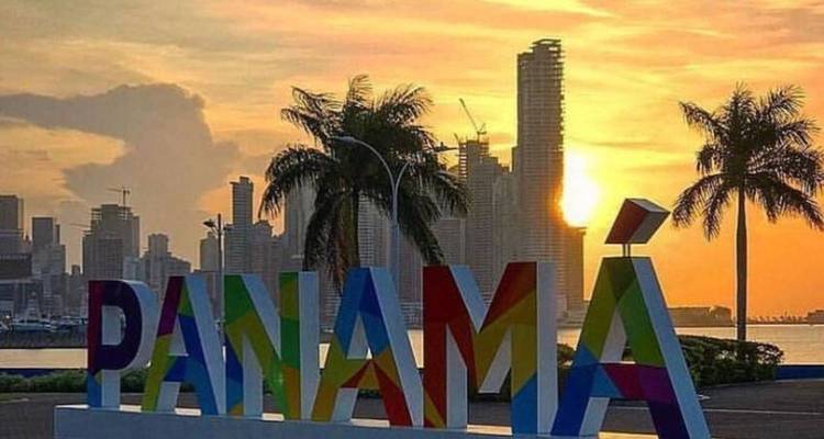 Colourful PANAMÁ letters stand before a modern skyline at sunset.
