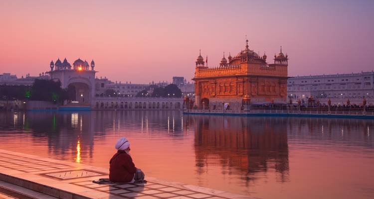 Un crépuscule rose tendre illumine le Temple d'Or se reflétant dans le bassin sacré tandis qu'un pèlerin solitaire est assis en contemplation.