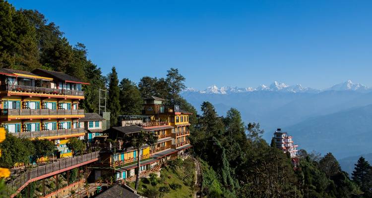 Colorful terraced hotels perched on a lush hillside overlook hazy Himalayan ranges on a clear day