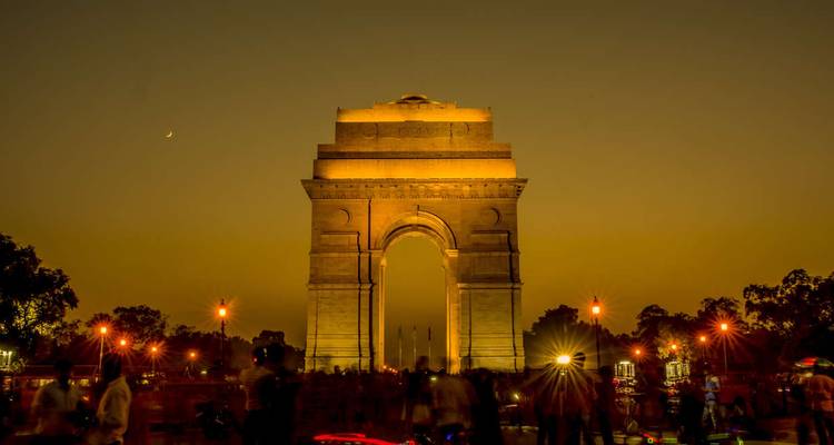 India Gate monument illuminated at dusk with silhouettes of evening crowds and streetlights.