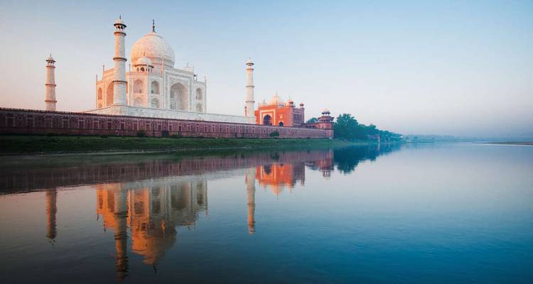 Iconic Taj Mahal reflecting in the calm Yamuna River during soft sunrise light.