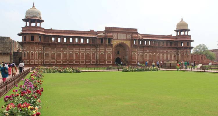 Wide view of red sandstone courtyard and ornate Mughal building with manicured lawn and flowers.