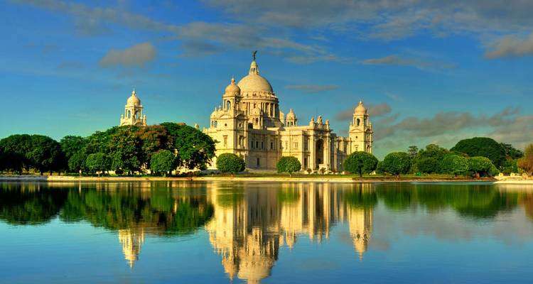 Grand marble Victoria Memorial reflected in tranquil water under vibrant evening sky.