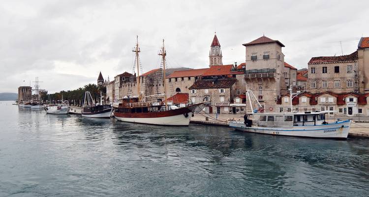 Waterfront en pierre de Trogir bordé de voiliers et de tours médiévales par un jour nuageux.