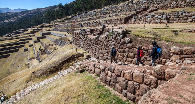 Trekkers descend terraced Inca ruins that cascade down a steep Andean hillside.