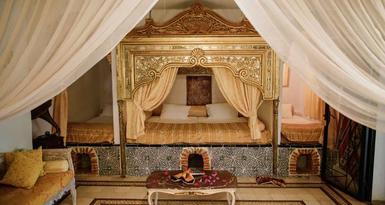 Luxuriöse tunesische Suite mit verziertem vergoldetem Himmelbett, Mosaikfliesen und fließenden weißen Vorhängen.