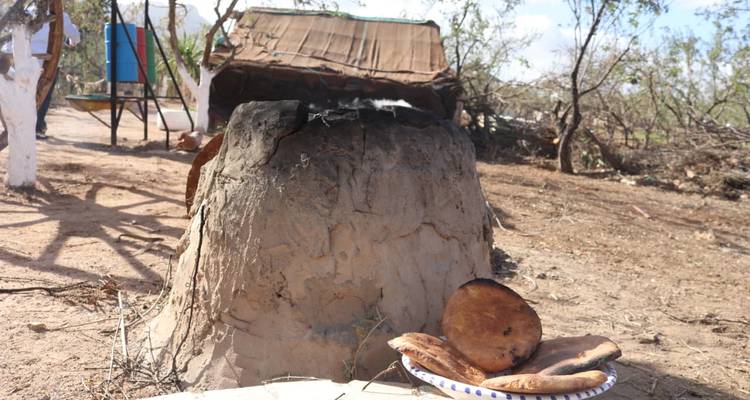 Traditioneller Lehmofen in trockener Landschaft mit frisch gebackenem Fladenbrot auf einem Teller.
