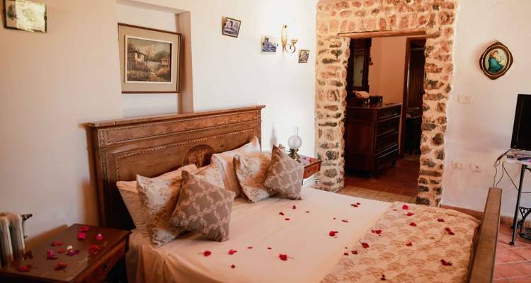 Charmantes rustikales Schlafzimmer mit Holzkopfteil, Steinwandakzenten und Rosenblättern auf der Tagesdecke.