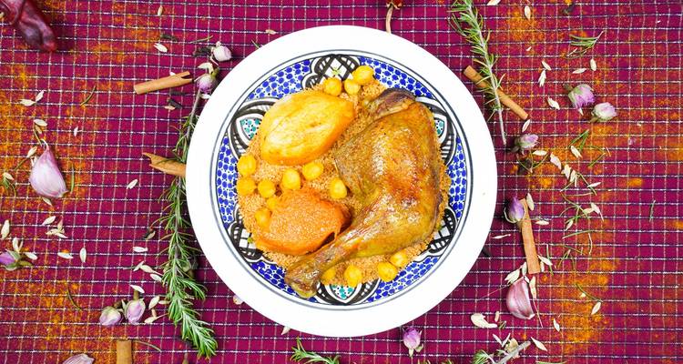 Vue plongée d'un tajine tunisien traditionnel de cuisse de poulet aux pois chiches et légumes dans une assiette à motifs.
