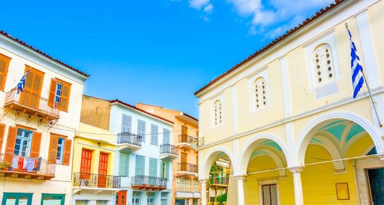 Bright neoclassical facades and Greek flag against vivid blue sky in old Nafplio streets.